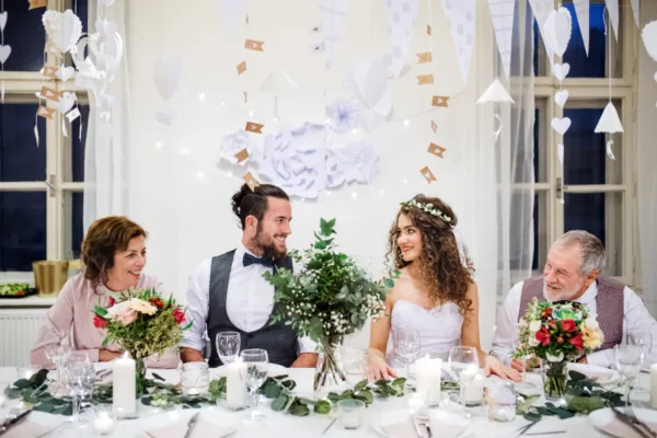 Bride and groom seated at a decorated head table indoors with family, showing why indoor and outdoor wedding venues differ in comfort and control.