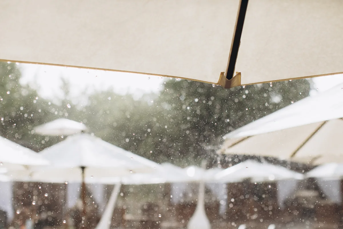 Indoor And Outdoor Wedding Venues: 9 Smart Differences Every Couple Should Know Rain falling over an outdoor reception setup with umbrellas, highlighting weather backup planning for weddings.